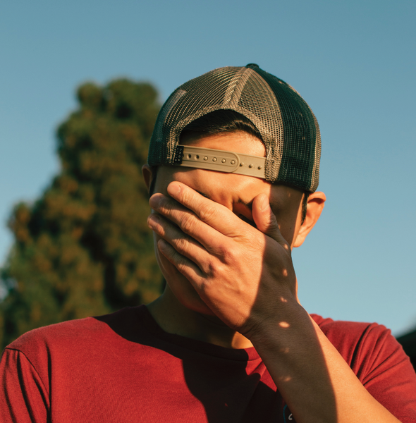 Young adult covering his face with his hand. While the sun shines on him.